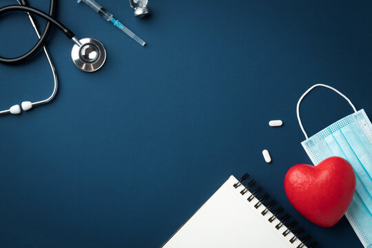 Red heart with doctor stethoscope, medical instruments and notebook on blue background, hospital life insurance concept, world heart health day. Copy space. Top view.
