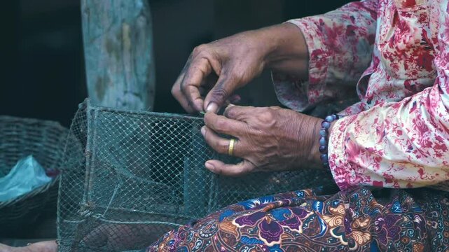 Old Khmer woman handcrafts a traditional Cambodian fish trap from of nylon thread wearing colorful&nbsp;clothes. Closeup. Slow mo, slow motion, high speed camera, 200fps
