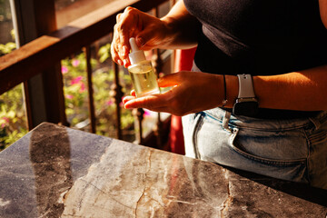 Female hands holding a glass bottle with natural oil for body and hair against the background of sunlight. Concept of natural cosmetics and face serum based on moisturizing oils
