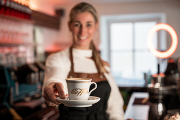 German barista with blonde hair serves a hot coffee drink to guest in a modern café
