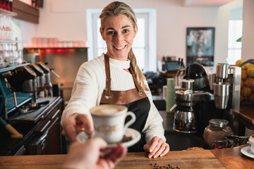 Young blonde woman serves coffee at a café bar with a welcoming smile