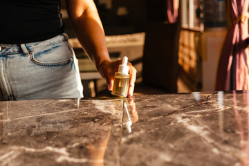 Female hands holding a glass clip with natural hair oil near a stone countertop in the rays of the sun. Concept of a serum for the skin of the face and body.