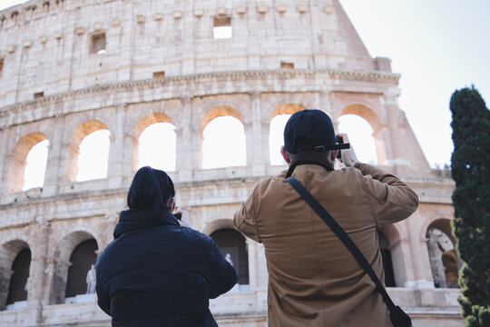 Two tourists capturing stunning images of the colosseum in rome, italy, while appreciating the rich history and architectural grandeur of this iconic ancient landmark