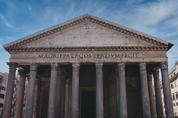 Low angle view of the pantheon's facade in rome, italy, showcasing classical architecture with corinthian columns, a triangular pediment, and the inscription under a vibrant blue sky