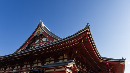 The roof of the main hall of Senso-ji Buddhist temple in Asakusa Tokyo with curved eaves and decorative elements stands out against the clear blue sky