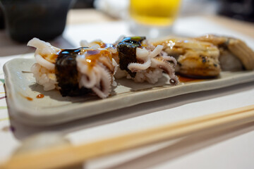 Japanese sushi featuring octopus nigiri wrapped in nori with a glossy sauce on a ceramic plate, highlighting fine culinary details and delicate seafood texture