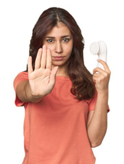 Middle Eastern woman with facial cleanser standing with outstretched hand showing stop sign,...