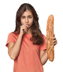 Middle Eastern woman holding bread loaf relaxed thinking about something looking at a copy space.