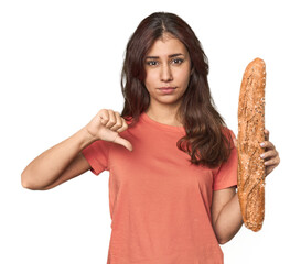 Middle Eastern woman holding bread loaf showing a dislike gesture, thumbs down. Disagreement...