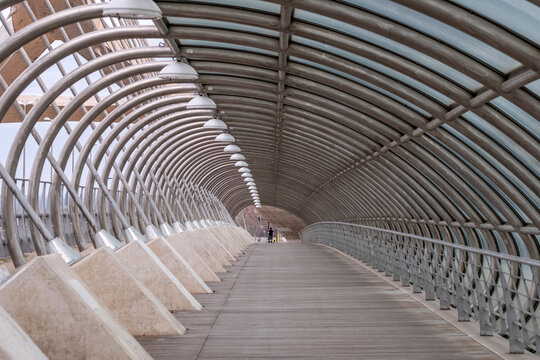 Curved pedestrian bridge tunnel with metal ribs and concrete pathway, representing modern urban engineering, symmetry and contemporary spatial design.