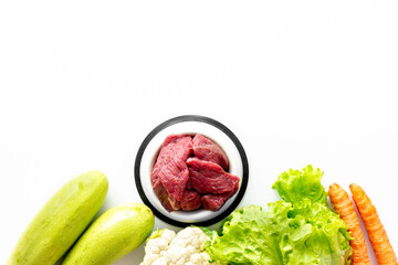 Natural pet food in feeding bowl and ingredients meat and vegetables, top view