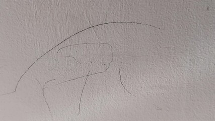 A toddler boy draws or scribbles with a black pen on the white wall. - Powered by Adobe