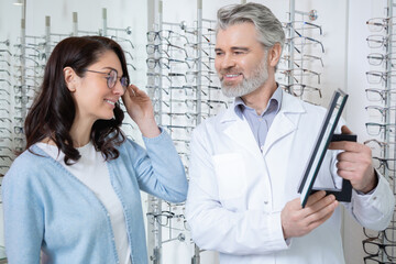 Woman choosing spectacles in optical shop with oculist