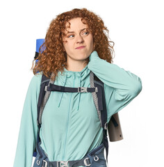 Young Caucasian redhead ready for hiking touching back of head, thinking and making a choice.