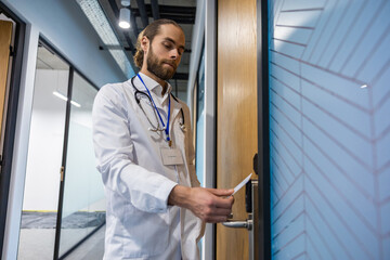 Man doctor pressing her access card on scanner at hospital door to open it
