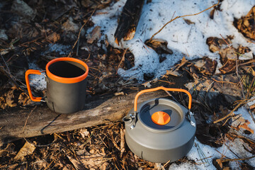 Two sturdy cups made of durable material and a kettle are neatly placed on the cold ground,...