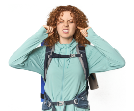 Young Caucasian redhead ready for hiking covering ears with fingers, stressed and desperate by a loudly ambient.