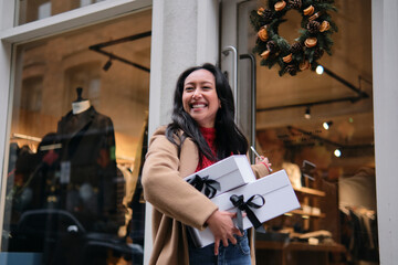 Woman smiling while holding gift boxes outside a store during holiday shopping