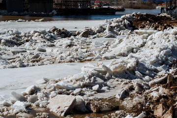 A substantial pile of ice is resting on the ground adjacent to a large body of water, creating a...