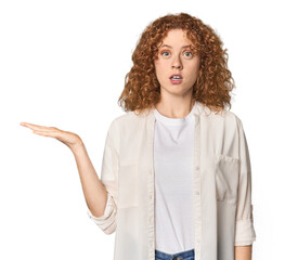 Young Caucasian redhead woman impressed holding copy space on palm.