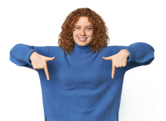 Young Caucasian redhead woman points down with fingers, positive feeling.