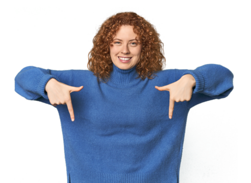 Young Caucasian redhead woman points down with fingers, positive feeling.