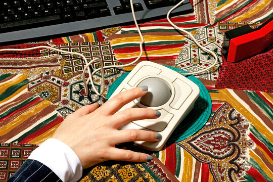 Hand using a trackball mouse on a colorful patterned tablecloth with a nostalgic 90s vibe