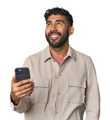 Hispanic male with mobile phone in studio dreaming of achieving goals and purposes