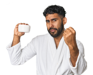 Hispanic male with moisturizer in studio showing fist to camera, aggressive facial expression.