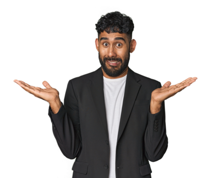 Hispanic businessman in suit in studio confused and doubtful shrugging shoulders to hold a copy space.