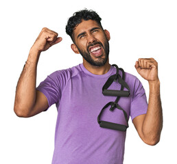 Hispanic male in sportswear with bands in studio raising fist after a victory, winner concept.