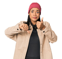 Young Filipino woman in studio showing thumbs up and thumbs down, difficult choose concept