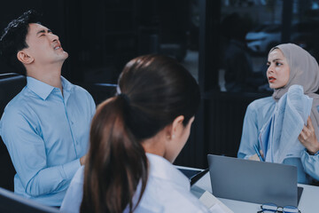 Young asian businesswoman suffering from headache while colleagues arguing and blaming her for bad...