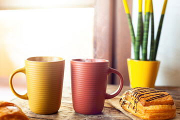 Steaming mugs and pastries enjoying morning sunlight near window