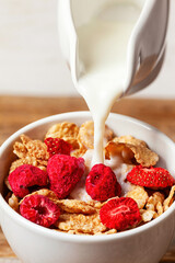 Pouring milk into bowl of cereals with dehydrated raspberries and strawberries for breakfast