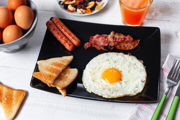 Delicious breakfast with fried egg, bacon, sausages and toasts on white wooden table