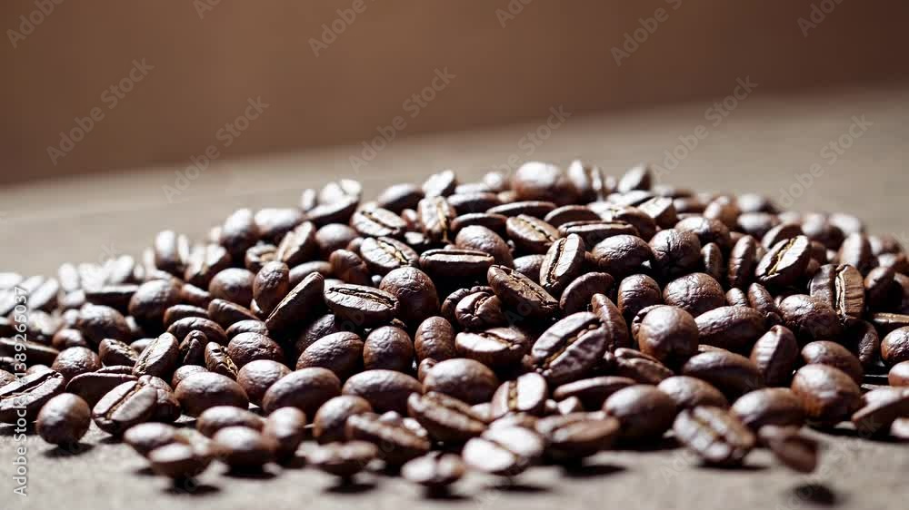 Poster close-up video of coffee beans falling onto a textured surface, captured from a low angle, emphasizi