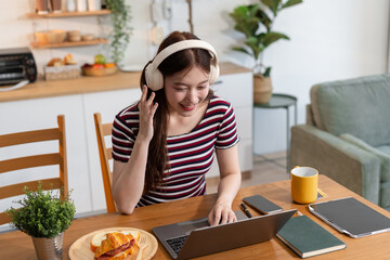 Smiling woman in headphones taking notes, motivated interested student studying online, using tablet, watching webinar training or listening to lecture, remote education concept.