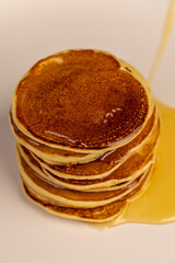 a tower of small milk pancakes on a ceramic bowl with natural yellow bee honey, closeup