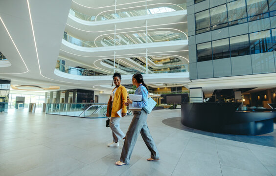 Two female corporate professionals walking in modern office lobby