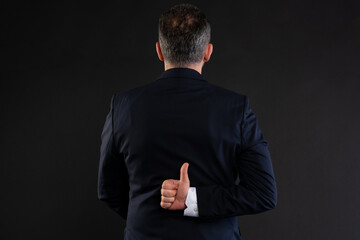 Businessman showing hidden thumbs up behind back.