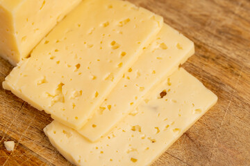 a piece of hard cheese with holes in place of slicing for cooking, pieces of sliced cheese on a cutting board, closeup