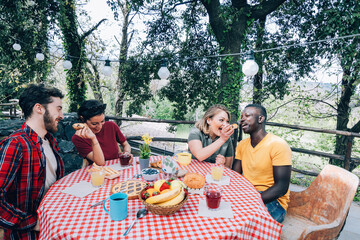 Happy friends enjoying meal outdoors at farmhouse table with red checkered tablecloth