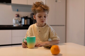 Young boy enjoying breakfast with a cup and fruit in a bright kitchen during morning hours
