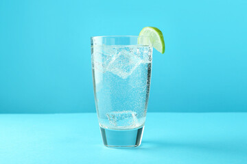 Soda water with lime and ice cubes in glass on light blue background