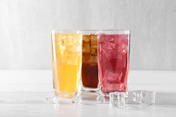 Soda water of different flavors in glasses with ice cubes on white wooden table