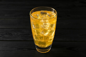 Sweet soda water with ice cubes in glass on black wooden table
