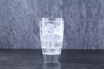 Refreshing soda water with ice cubes in glass on grey table