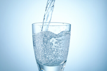 Pouring refreshing soda water into glass on light background, closeup