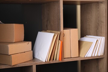 Different paper envelopes and parcels on wooden shelves in post office